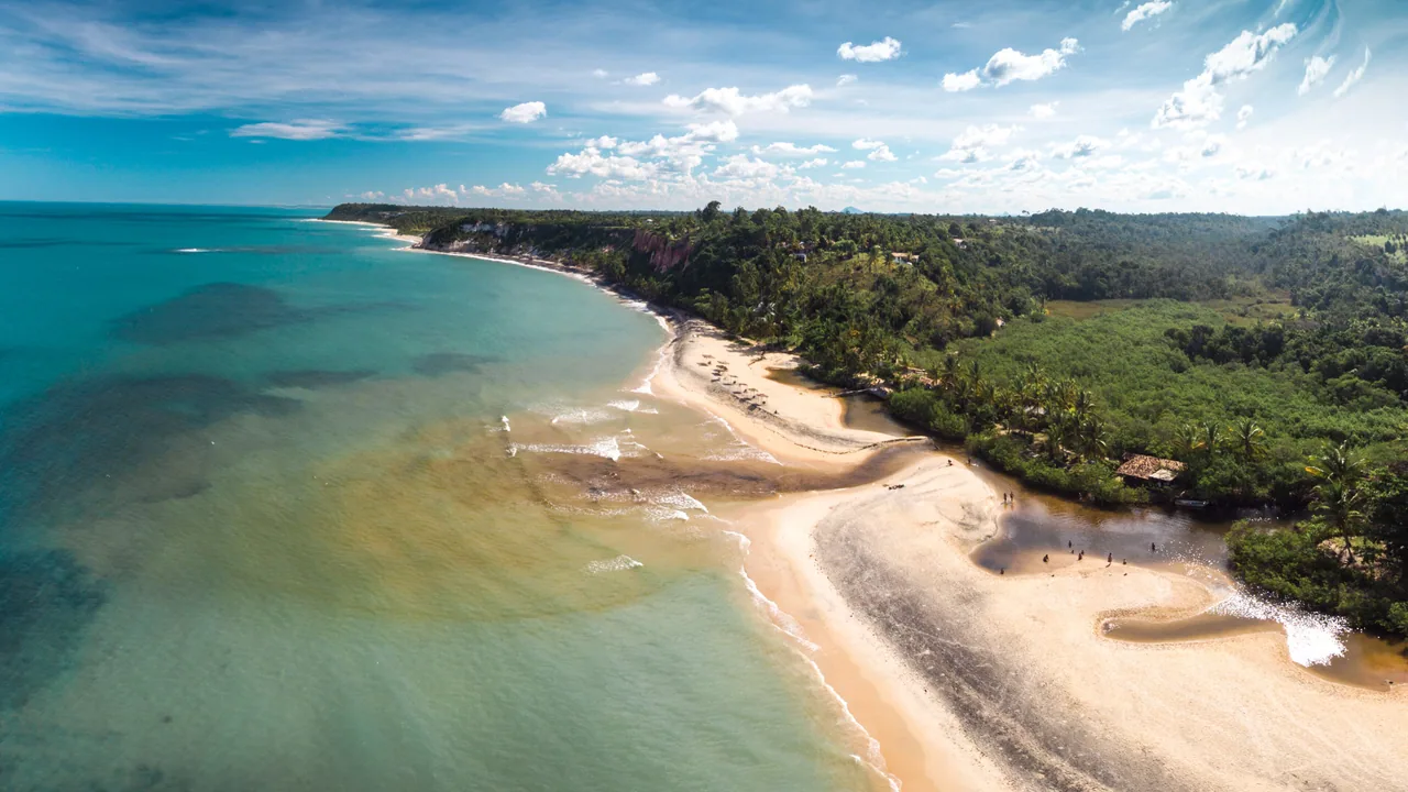 Vista aérea da Praia do Espelho, com faixa de areia, vegetação e recifes sob a água.