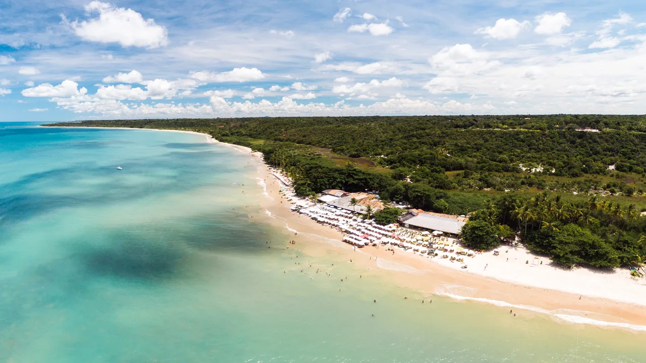 Vista aérea da Praia dos Coqueiros, em Trancoso, com mar azul-esverdeado.